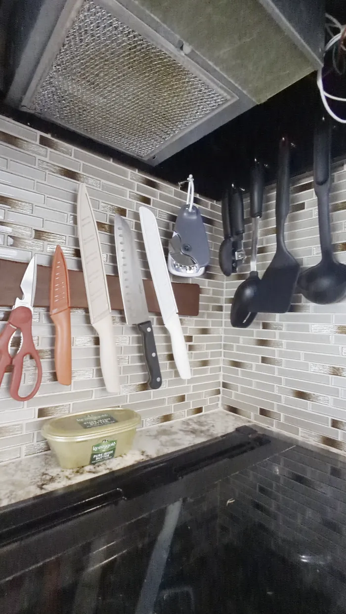 The cooktop, with knives and utensils on the wall above it