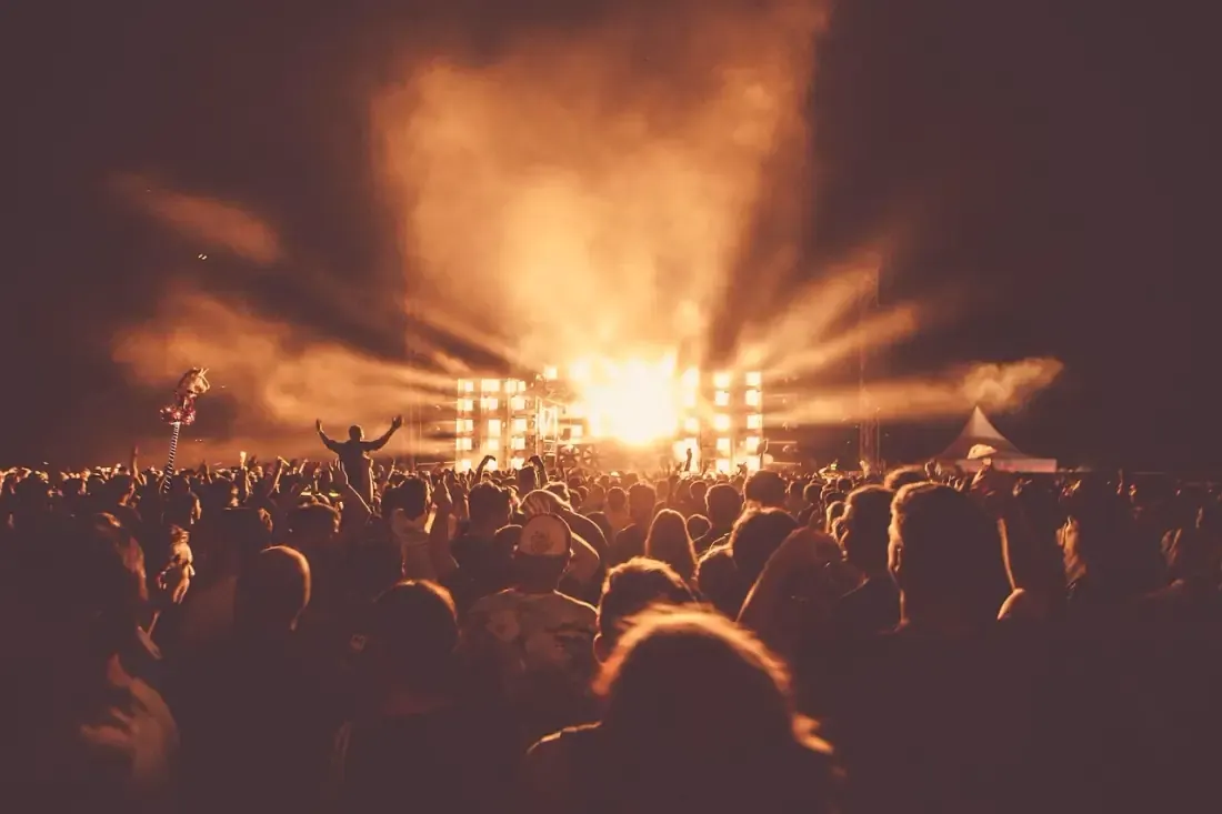 Outdoor festival crowd facing a lit stage at dusk