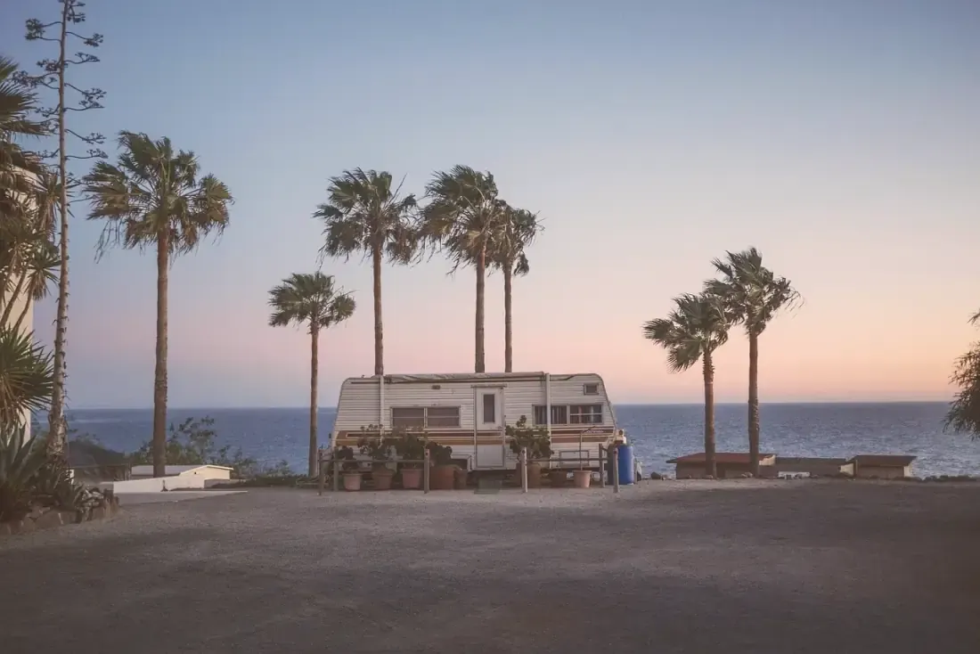 Travel trailer parked by the sea under palm trees at dusk